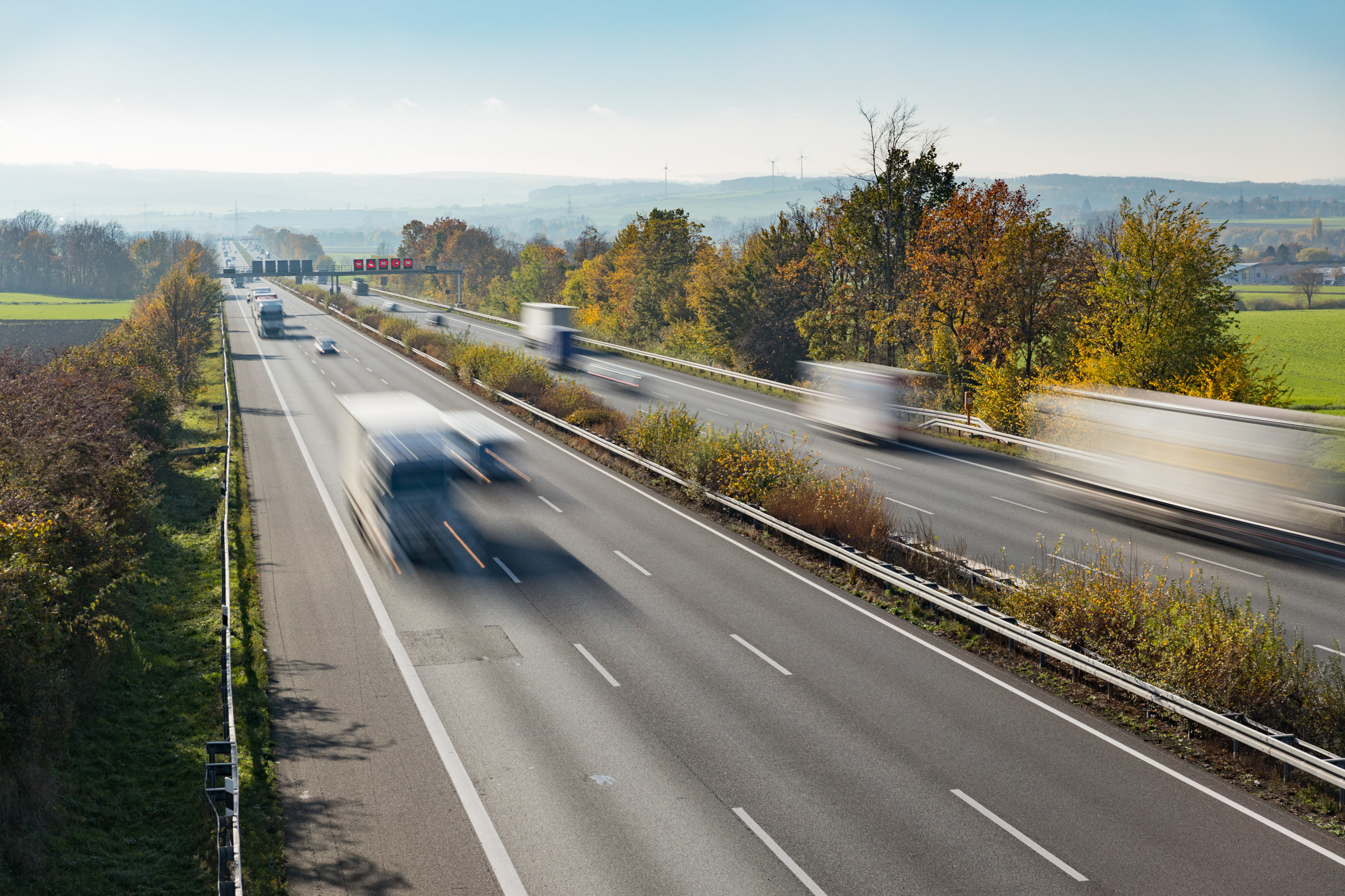 Autobahn in Vogelperspektive mit bewegungsunscharfen Fahrzeugen umgeben von grüner Landschaft