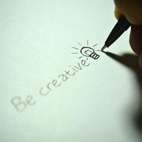 Ein Stift schreibt "be creative" auf ein Blatt Papier