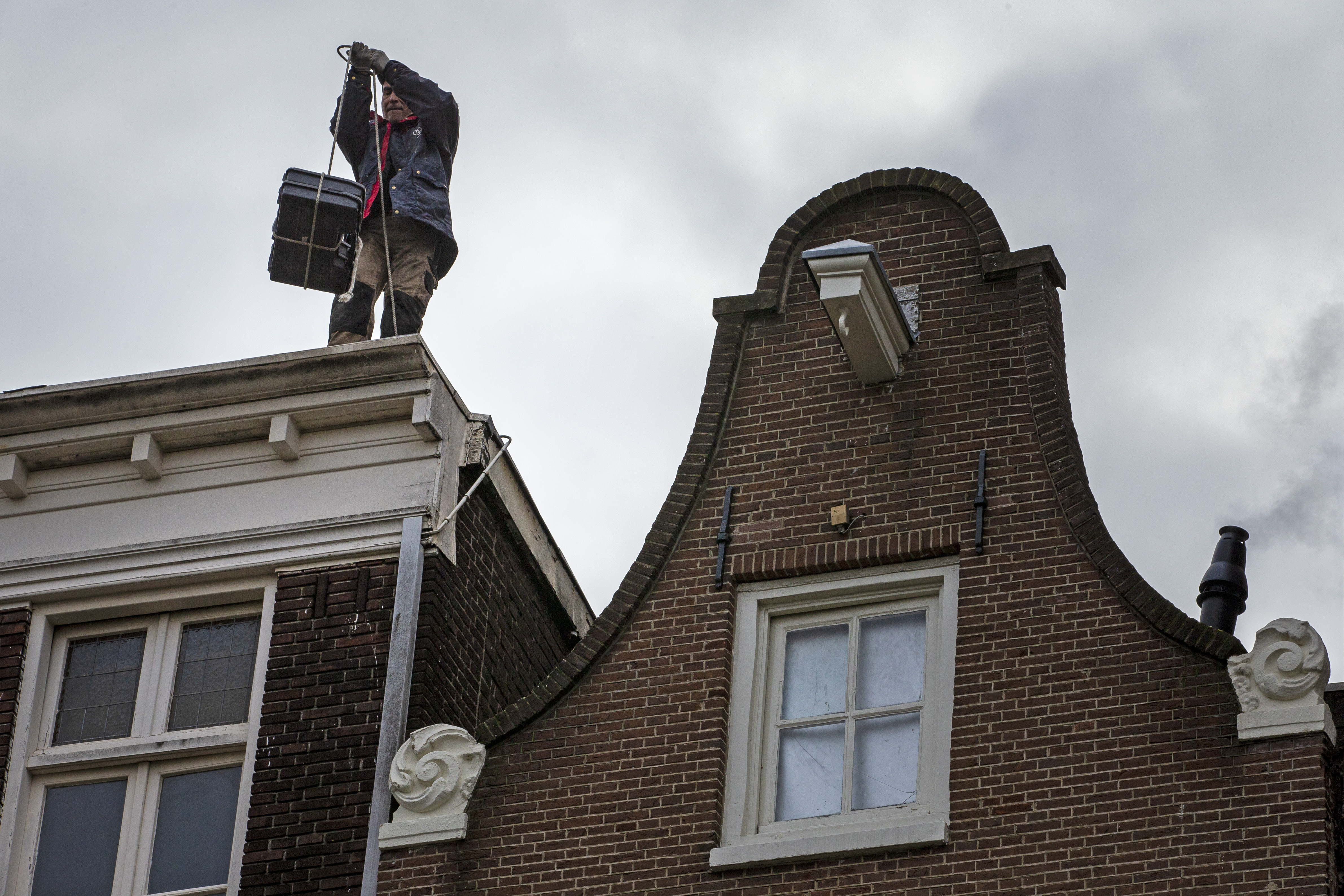 Eine Person steht auf dem Dach eines Hauses und nimmt eine Plastikkiste entgegen