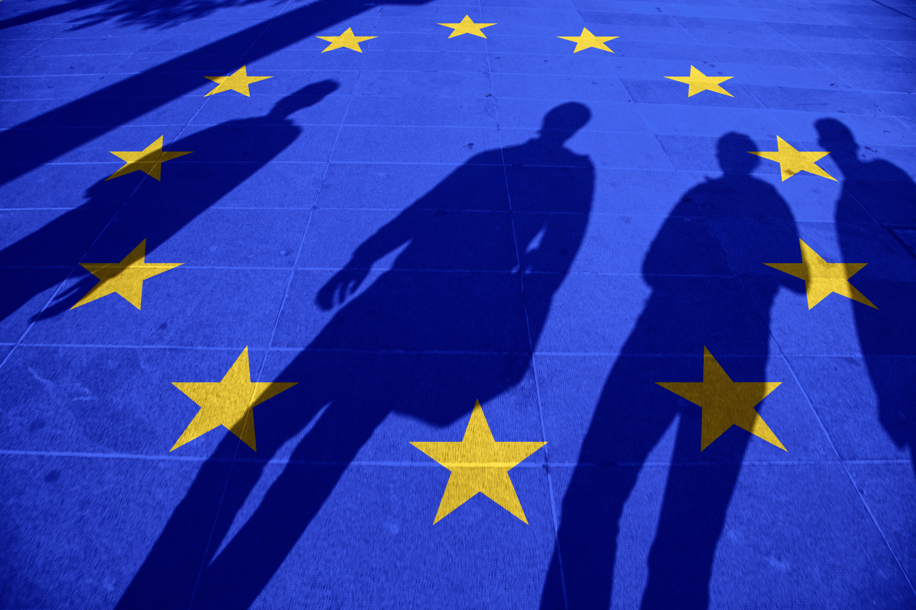 Blauer Boden mit im Kreis verlaufenden gelben Sterne, die Flagge der Europäischen Union symbolisierend, Schattenumrisse von vier Personen erkennbar