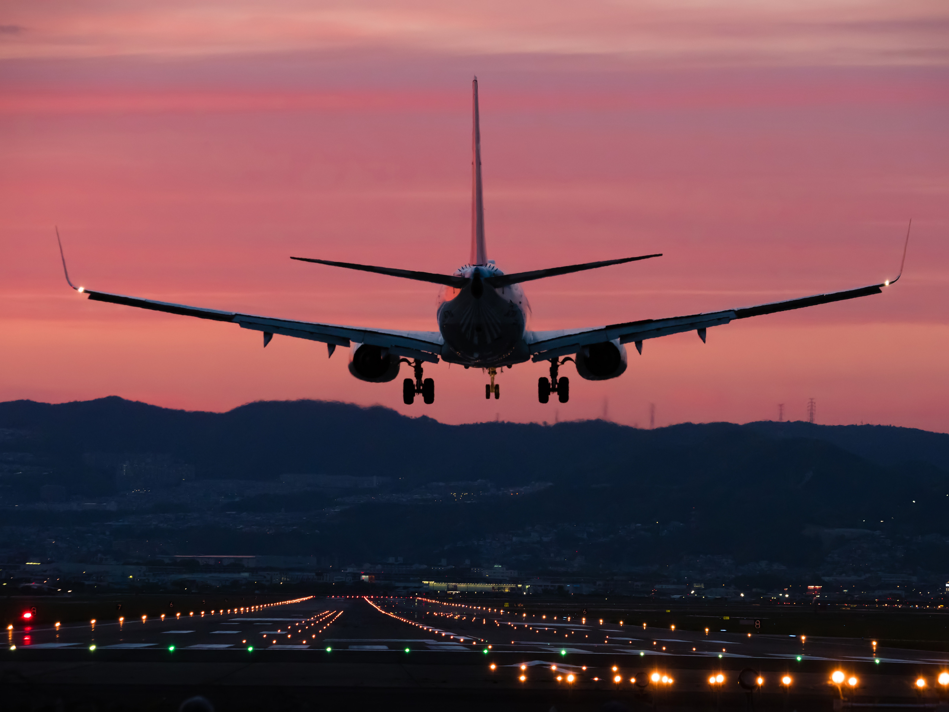 Flugzeug in Rückansicht bei Landung auf beleuchtete Landebahn im Abendrot