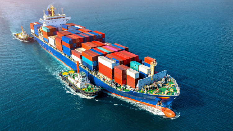 Beladenes Frachtschiff mit Containern wird auf offenem Meer von zwei weiteren Schiffen begleitet
