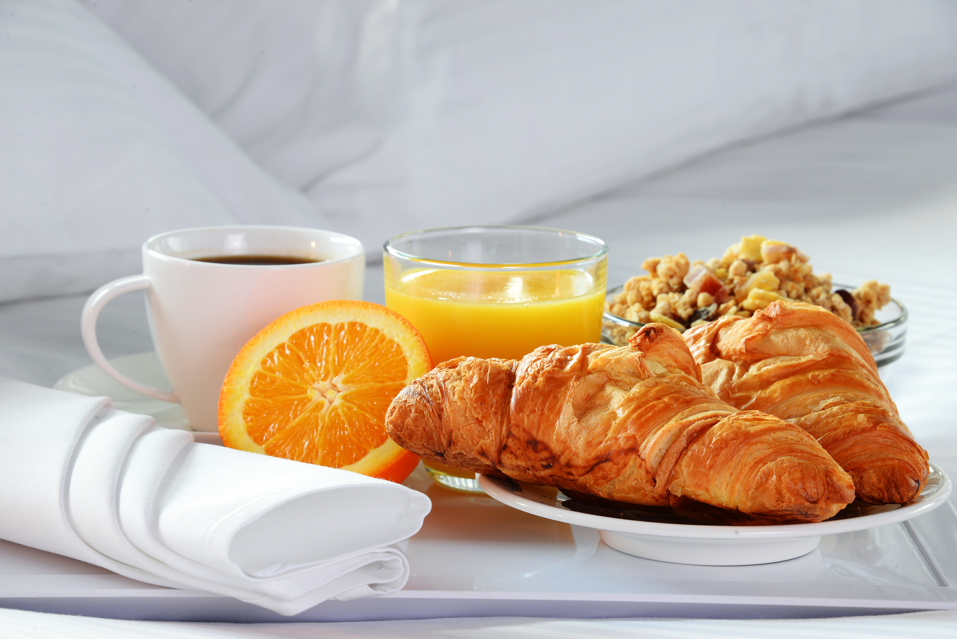 Frühstück mit Kaffee, einem Glas Orangensaft Müsli und Croissants auf einem Tablett in einem Bett platziert