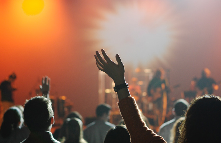 erhobene Hand im Vordergrund, im Hintergrund Konzertbühne