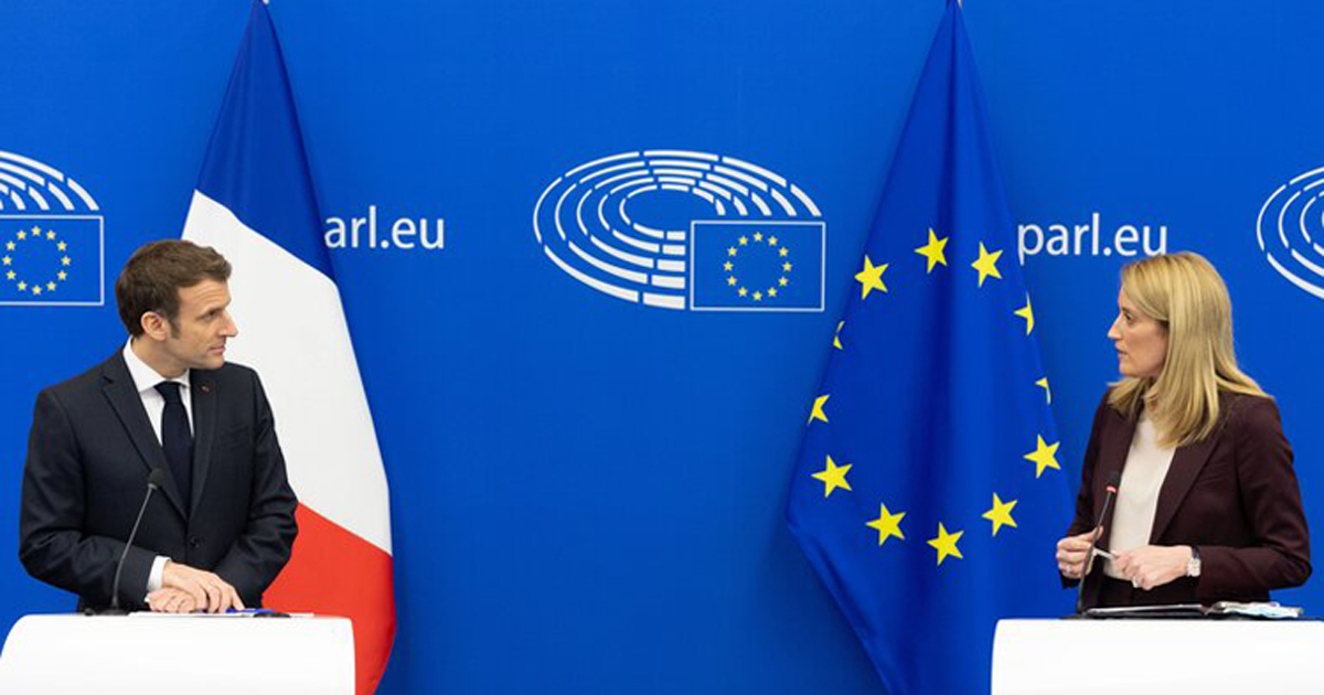 Präsident Macron und Roberta Metsola im Gespräch, im Hintergrund Europaflagge