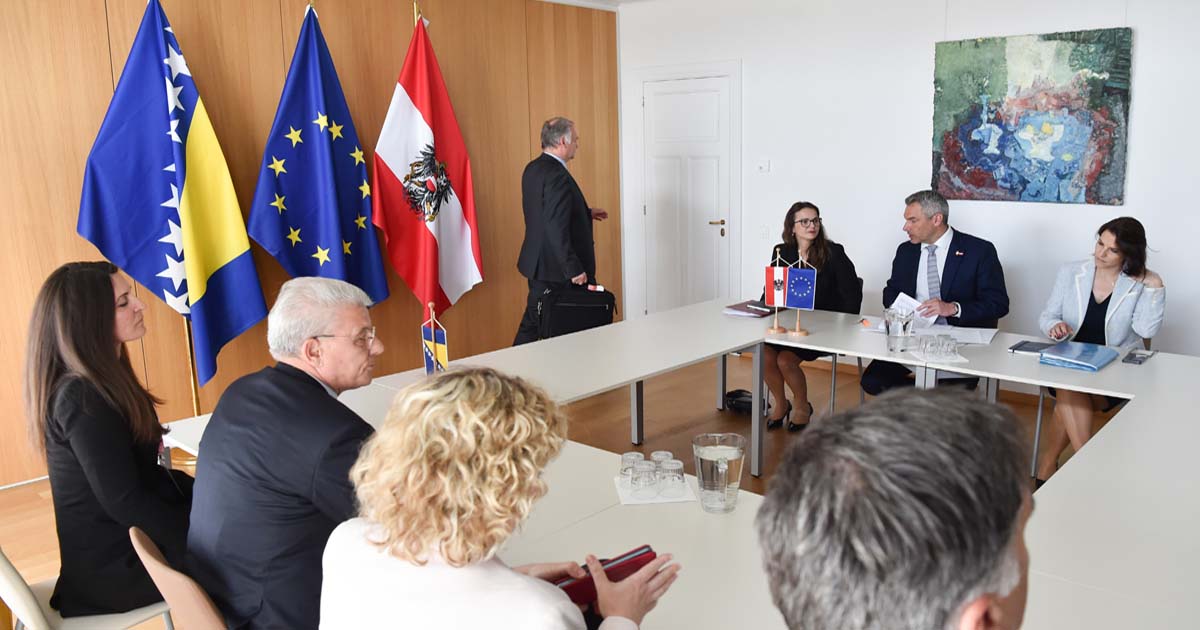 Eine Gruppe Politiker:innen in einem Sitzungsraum vor Flaggen