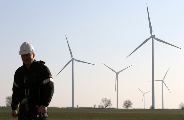 Ein Arbeiter mit Helm, im Vordergrund, im Hintergrund Windräder