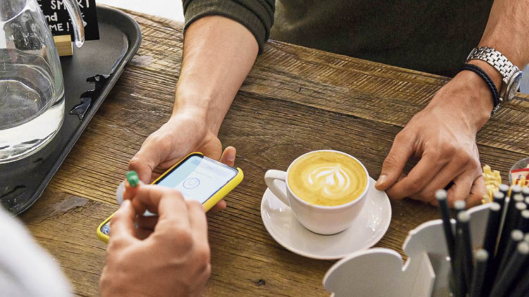Ein Kunde kauft eine Kaffe und hält sein Handy hin, damit es digital abgestempelt wird. 